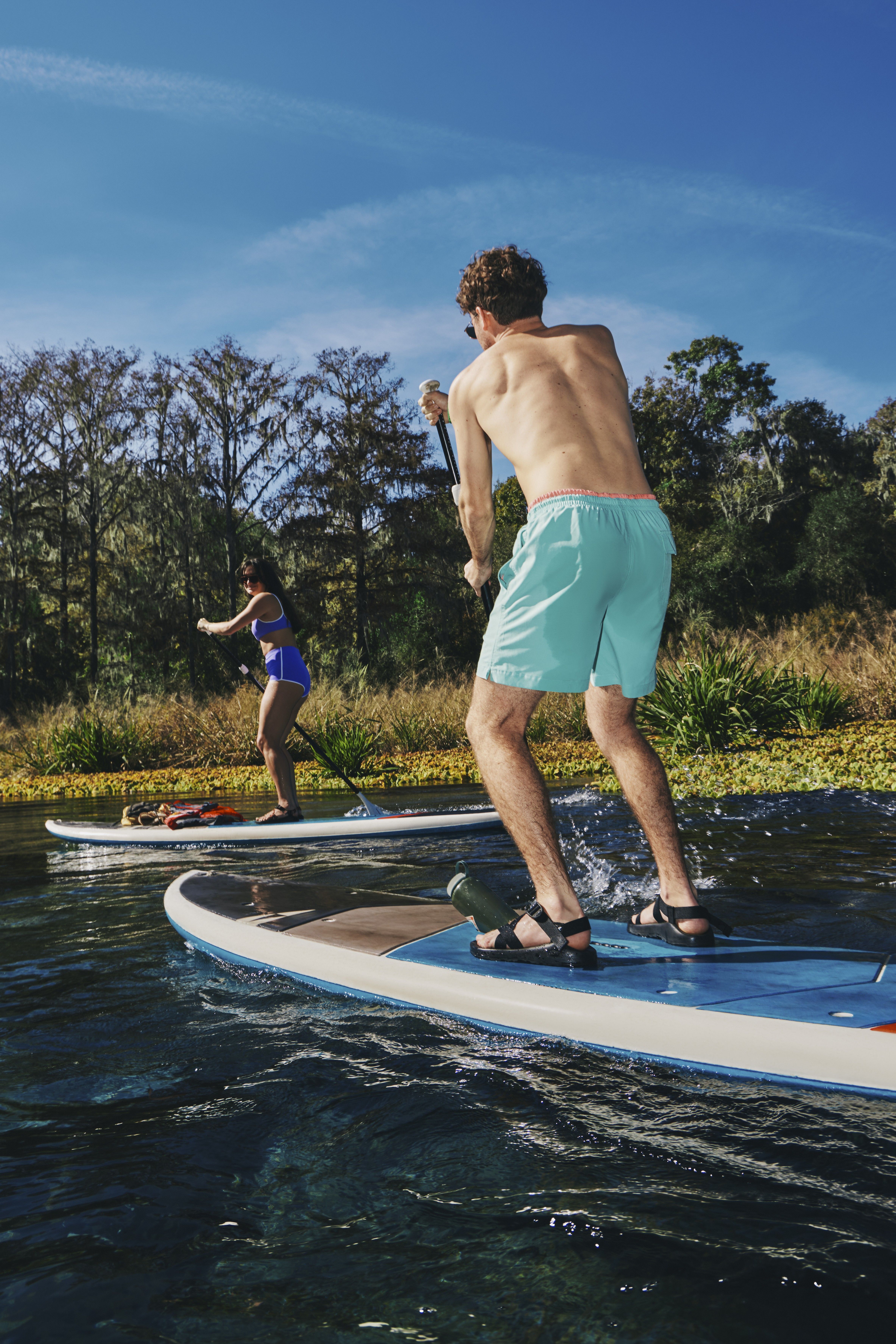 Two people paddleboarding on a calm lake under a clear blue sky.
