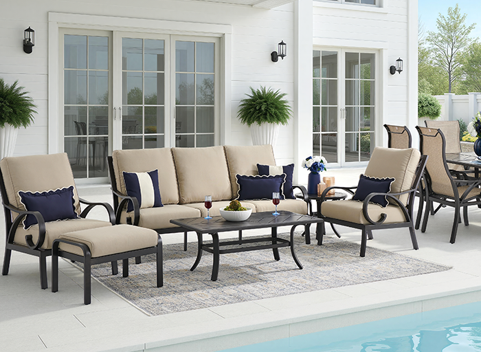Outdoor seating area by a pool with beige cushions and decorative pillows.