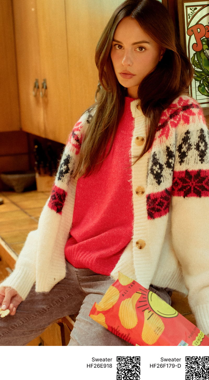 Young woman in colorful sweater and patterned bag, posing indoors.