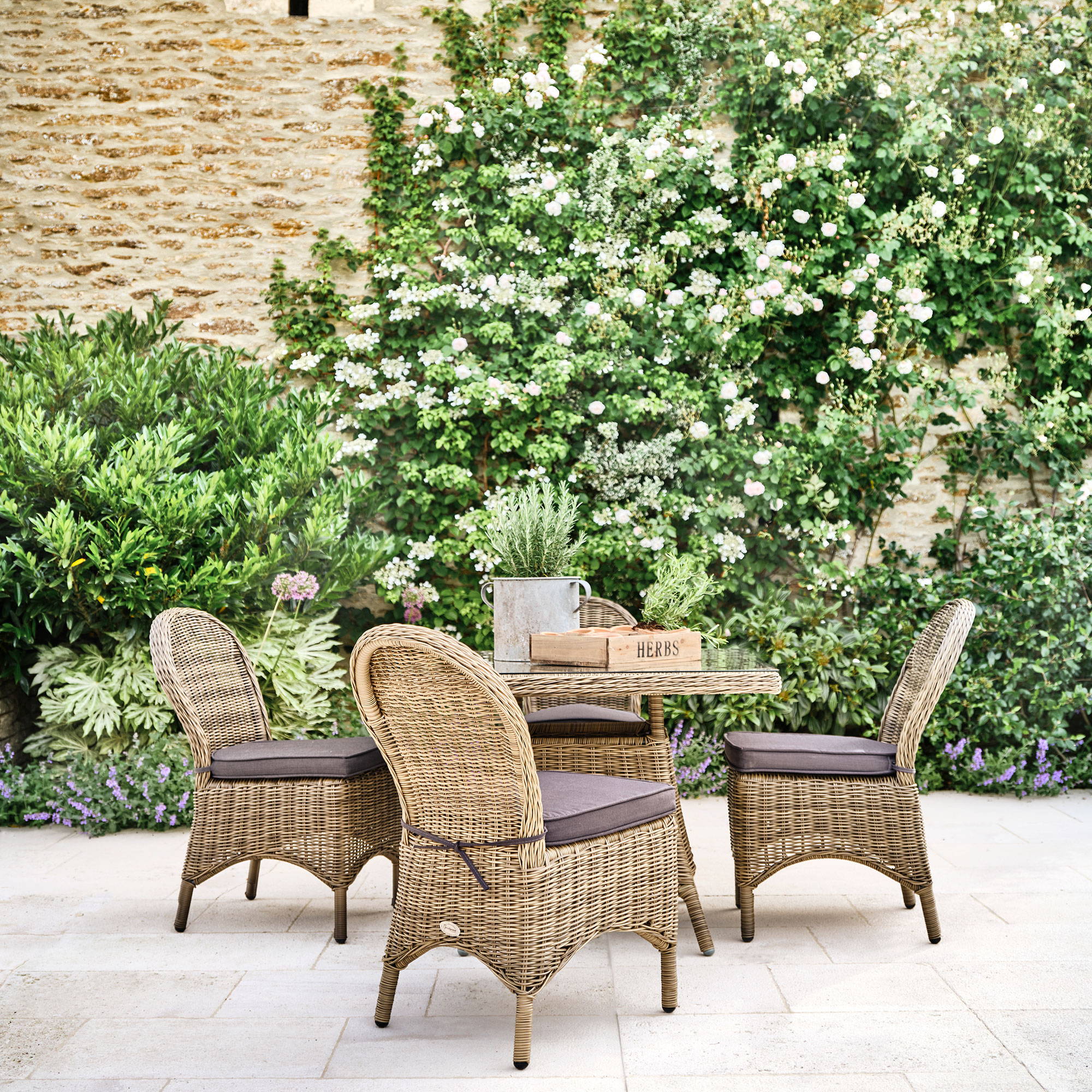 Natural rattan dining set on a patio in front of a wall of ivy and lavendar.