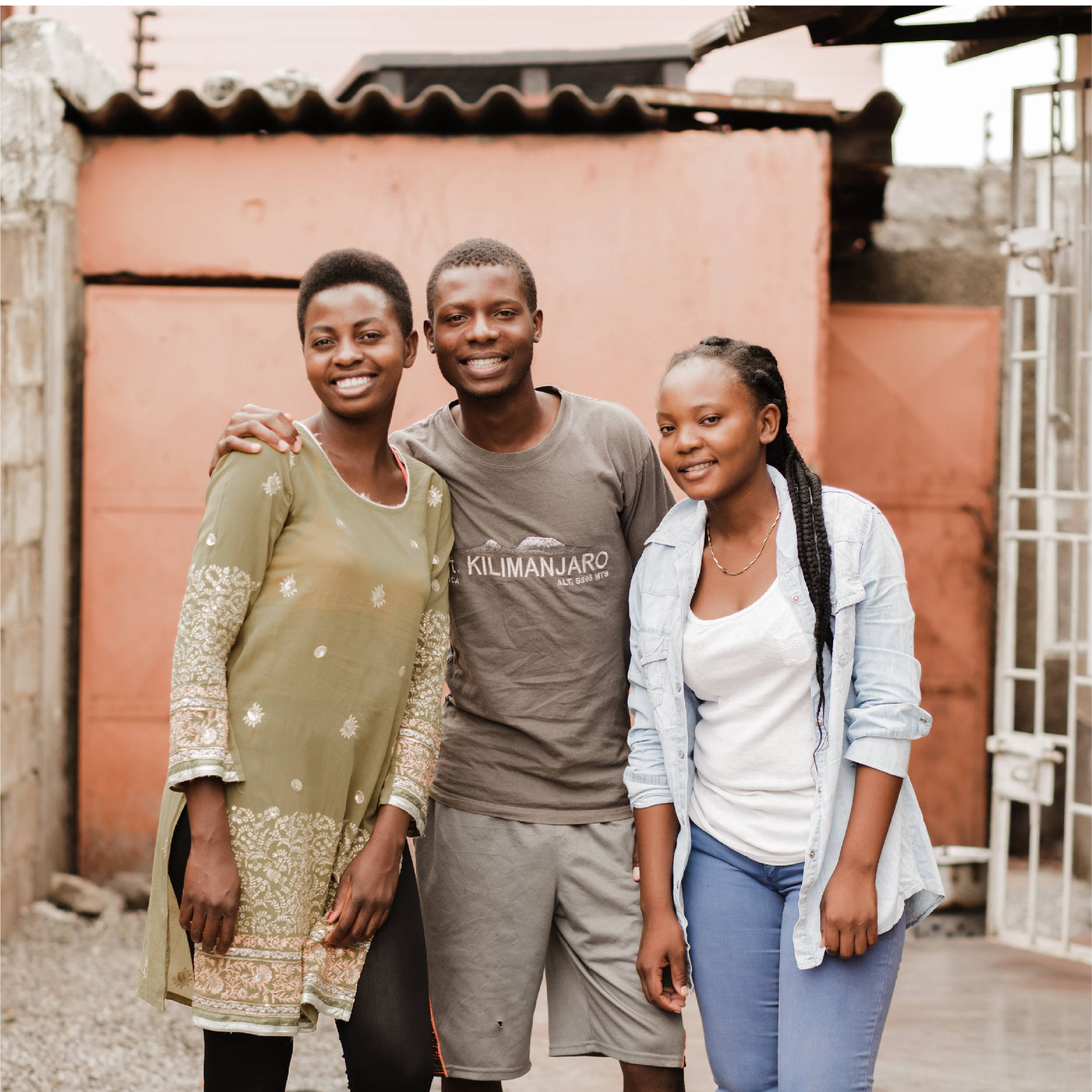 three young adults in Zambia (two girls and a guy) pose with their arms around each other and smile