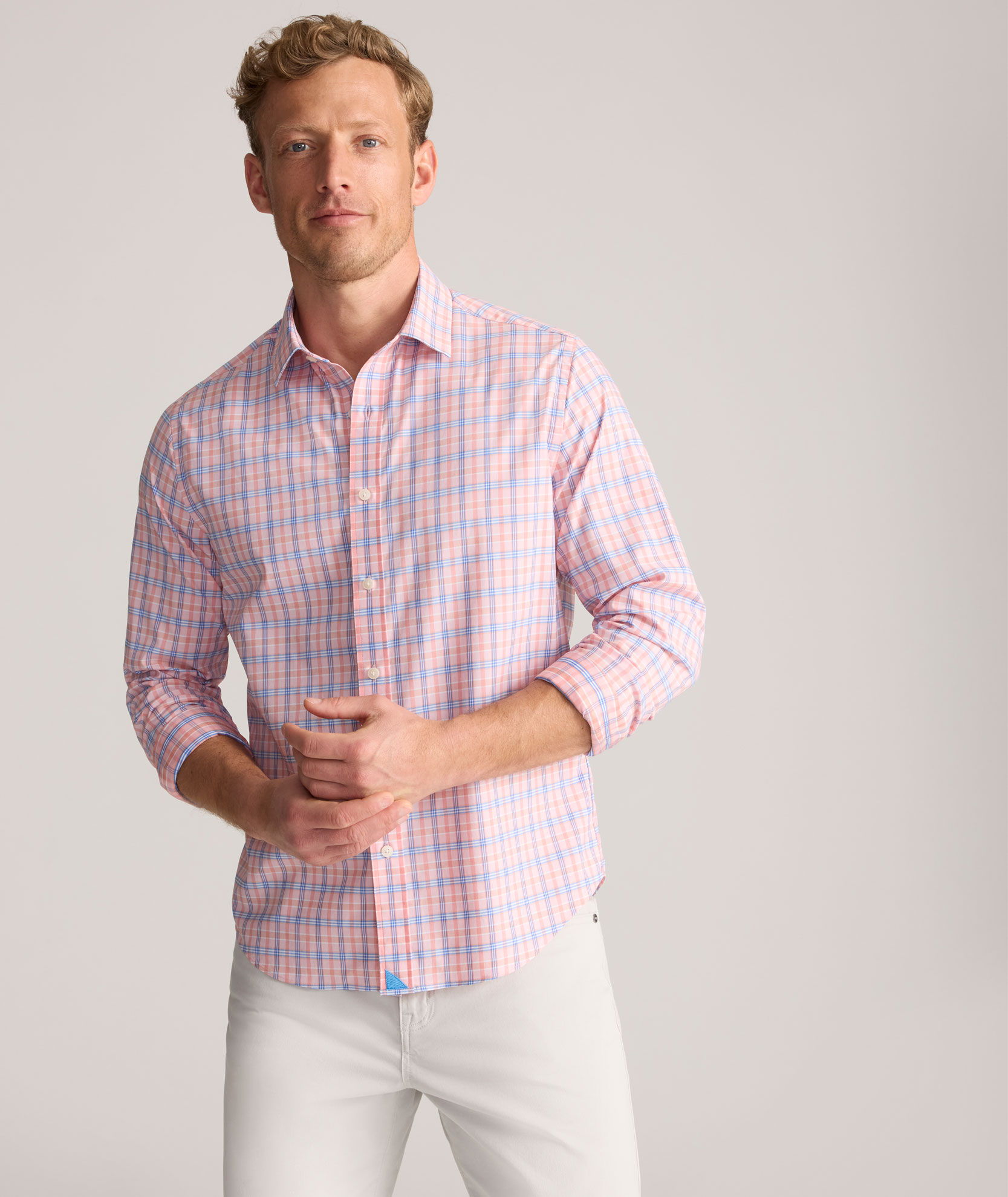 Man in a checkered shirt and white pants, posing against a neutral background.