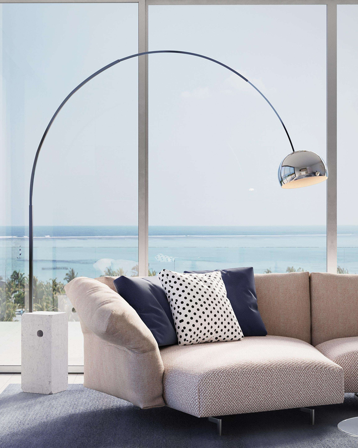 Modern living room with curved Arco lamp, sofa, and ocean view.