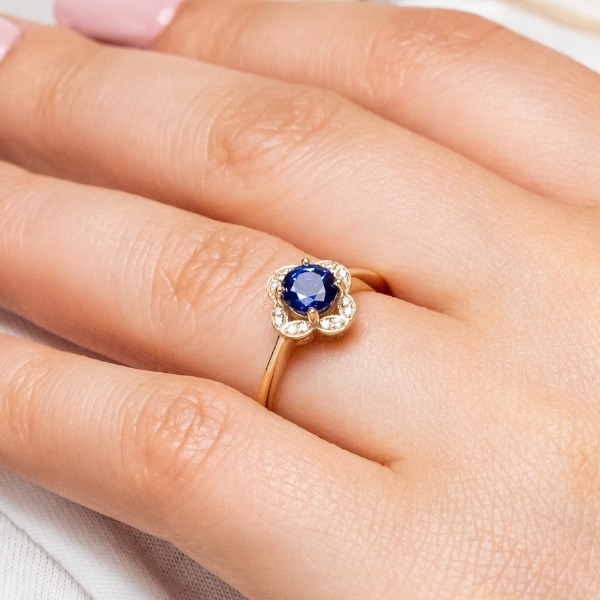 a nature inspired ring with a simple floral pattern accented with diamonds featuring a round cut blue sapphire at the center