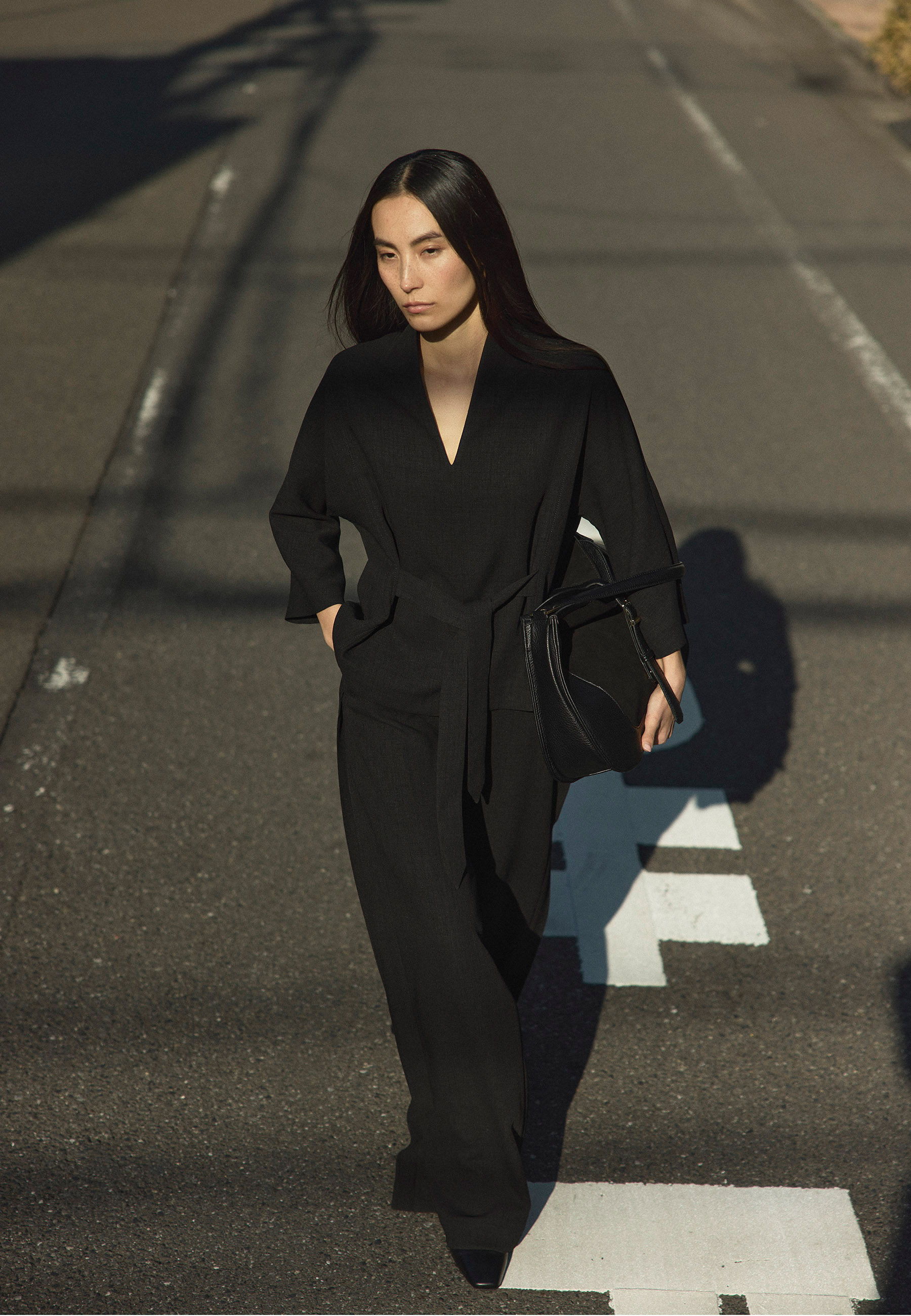 A woman in a black outfit walking on a street.