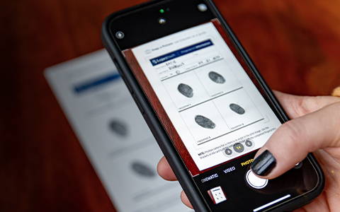 person holding a smartphone taking a picture of inked fingerprints