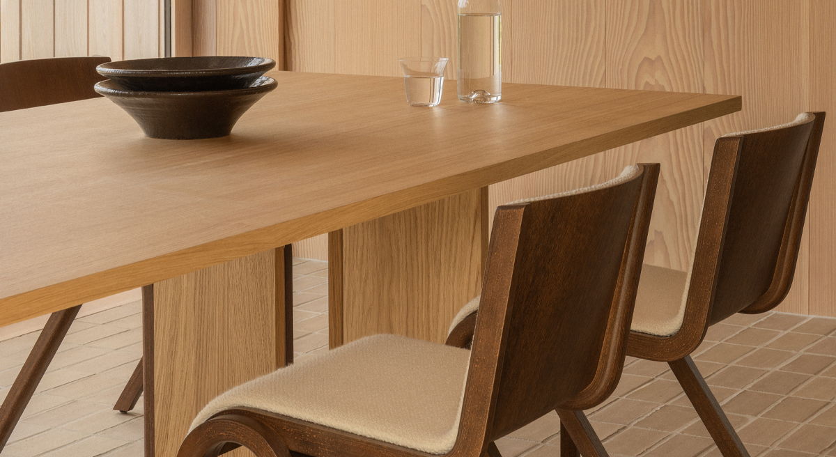 A wooden Audo Copenhagen dining table with two chairs and a bowl.