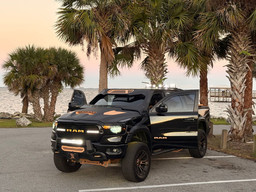 Front three-quarter view Pedro's 2021 Ram Bighorn 1500 lifted black truck with LED light bar and bronze accents Conductor's Special 232 Spare Tire Delete HornBlasters featured install gallery photo 1