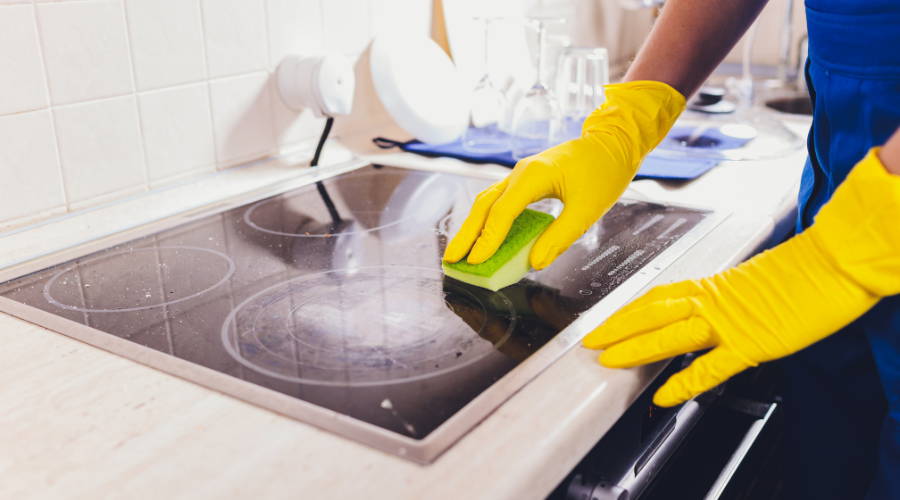 person with yellow gloves on cleaning a glass stovetop