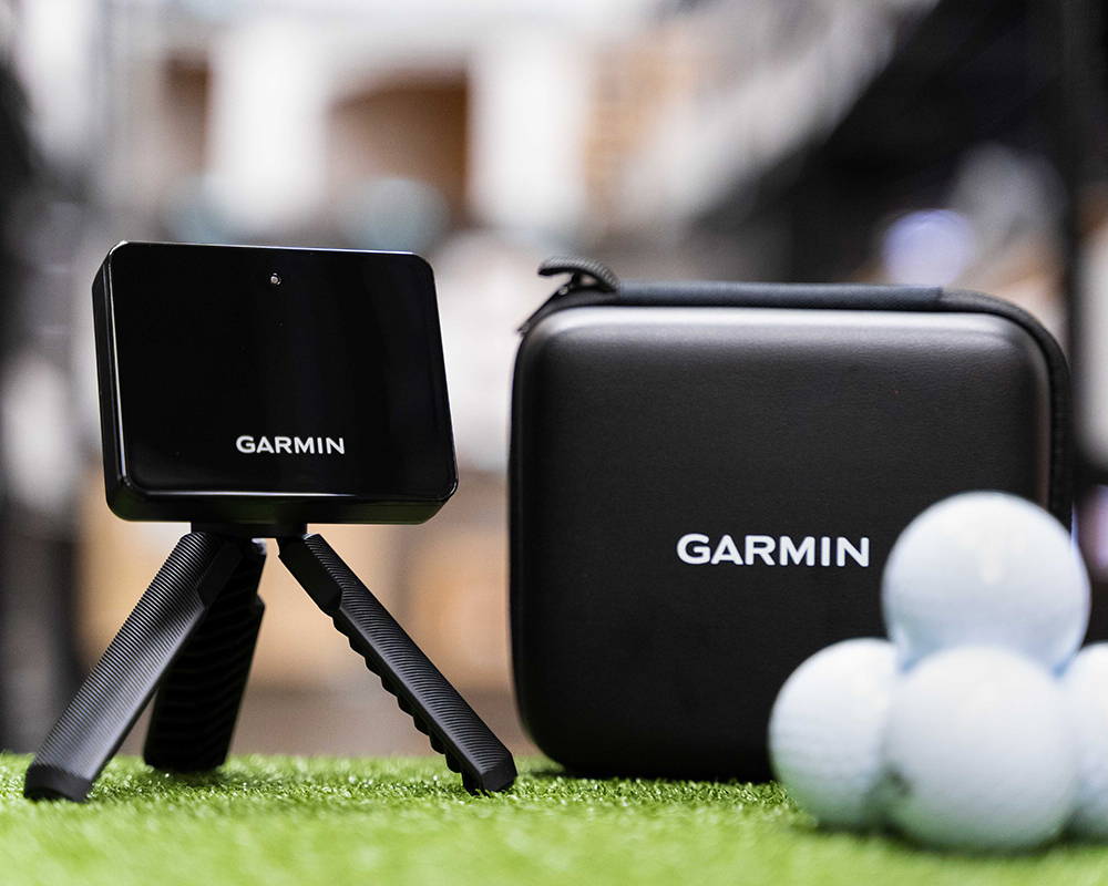 The Garmin Approach R10 golf launch monitor next to the carrying case and stack of golf balls