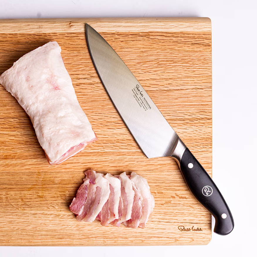 Knife and sliced meat on a wooden cutting board.