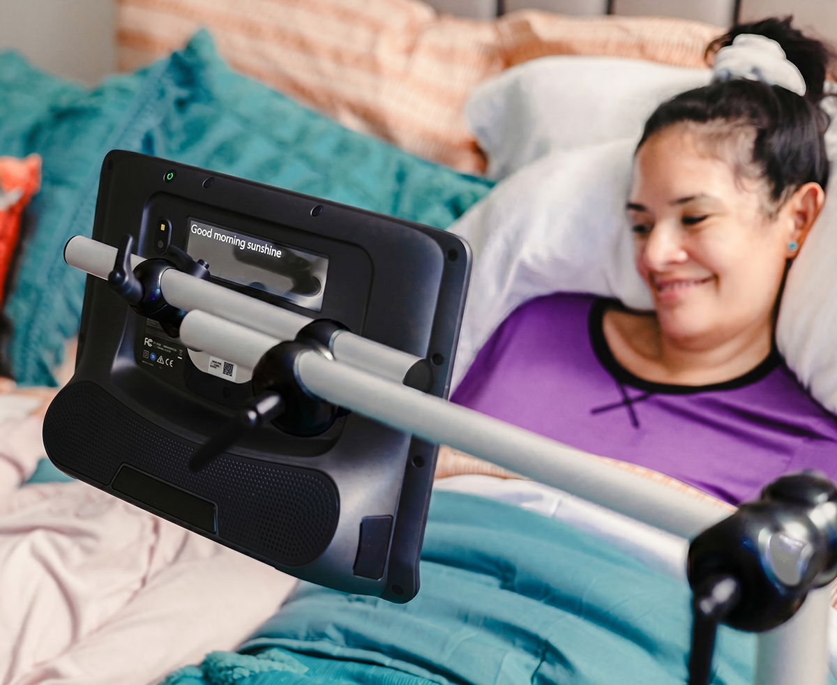 Floorstand mount for a Tobii Dynavox assistive communication device used by a woman in her bed