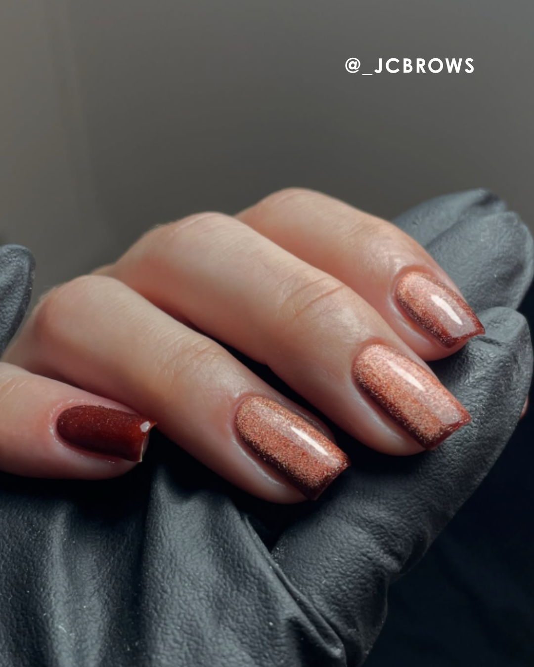 A hand with stylish nail polish on a black leather surface.