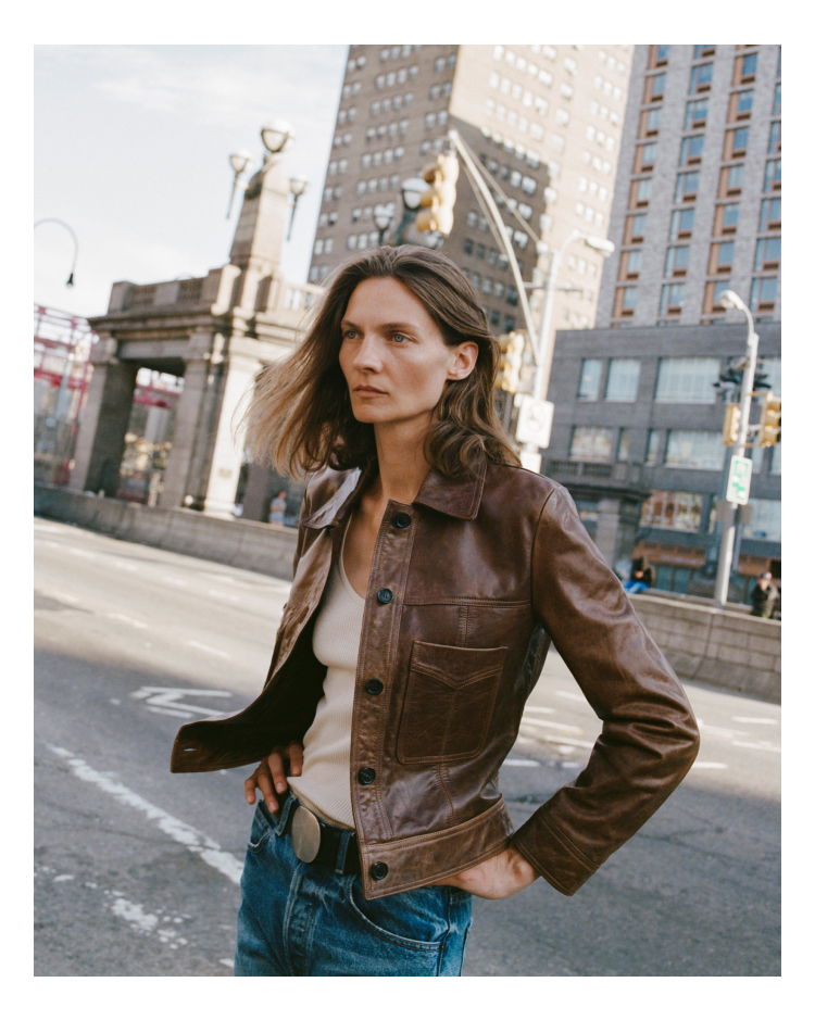 Person wearing a brown jacket standing on a city street.