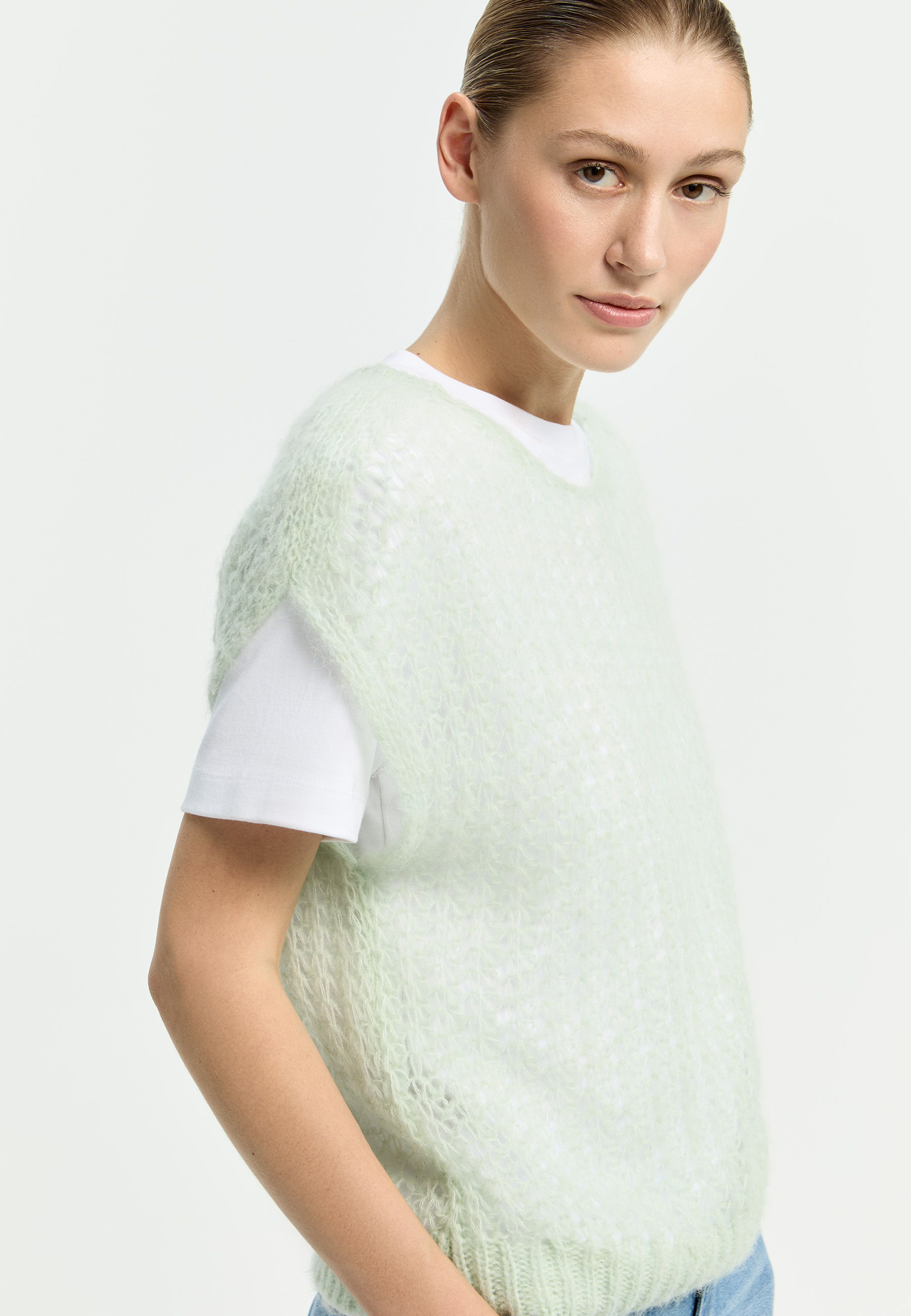 A woman wearing a light green sweater over a white shirt.