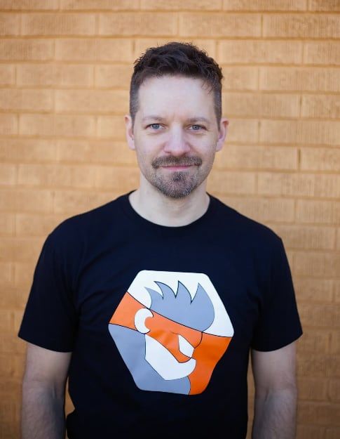 Man standing in front of a brick wall, wearing a graphic t-shirt.