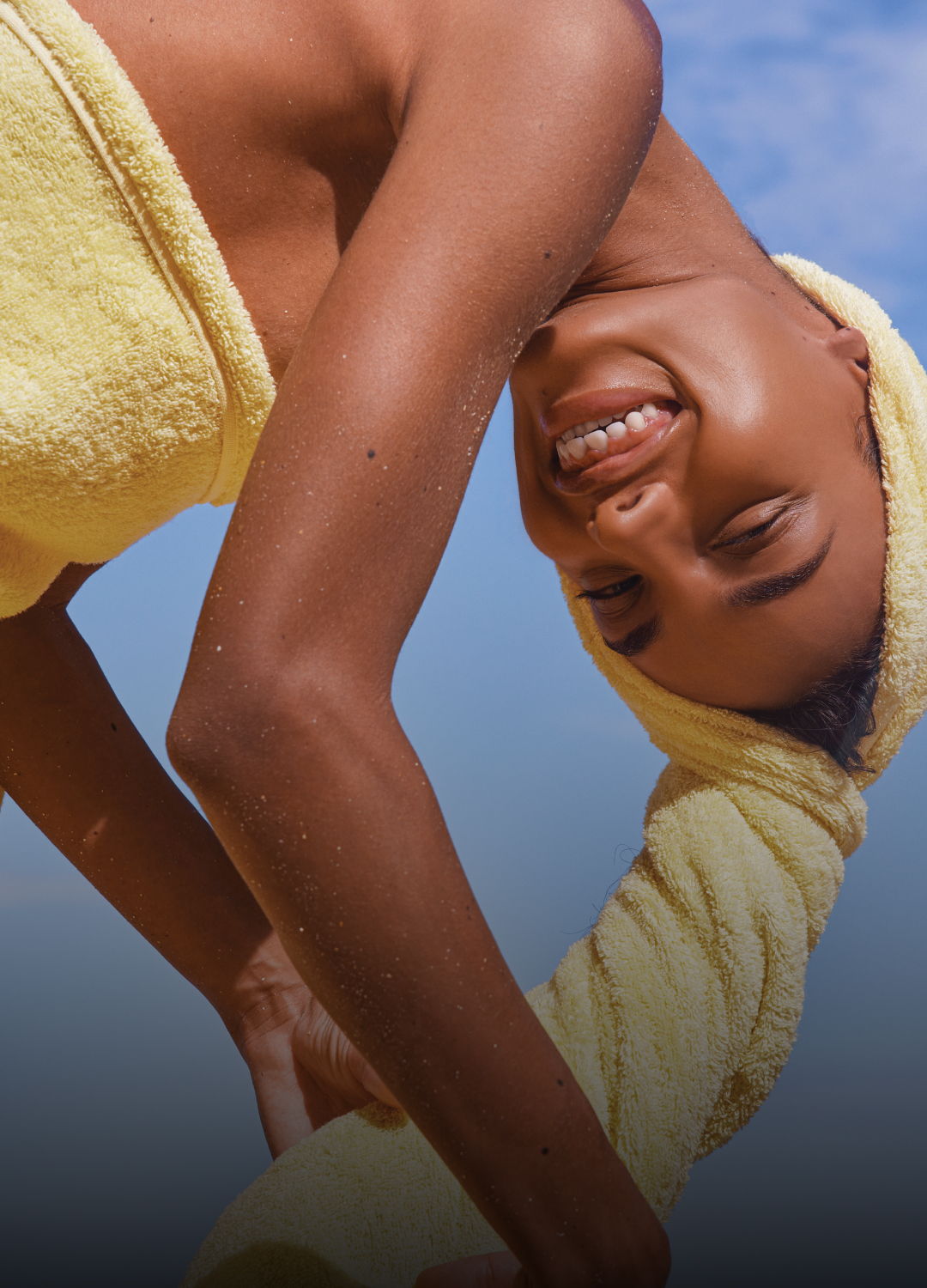 Smiling person with a towel, posing against a blue sky background.