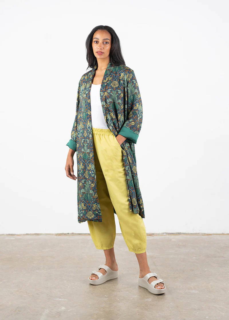 A model wearing a long, green botanical jacket gown over a white top, yellow trousers and off white chunky slides