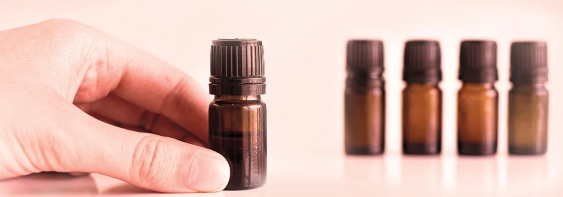 Hand holding a brown essential oil bottle with more bottles in the background.