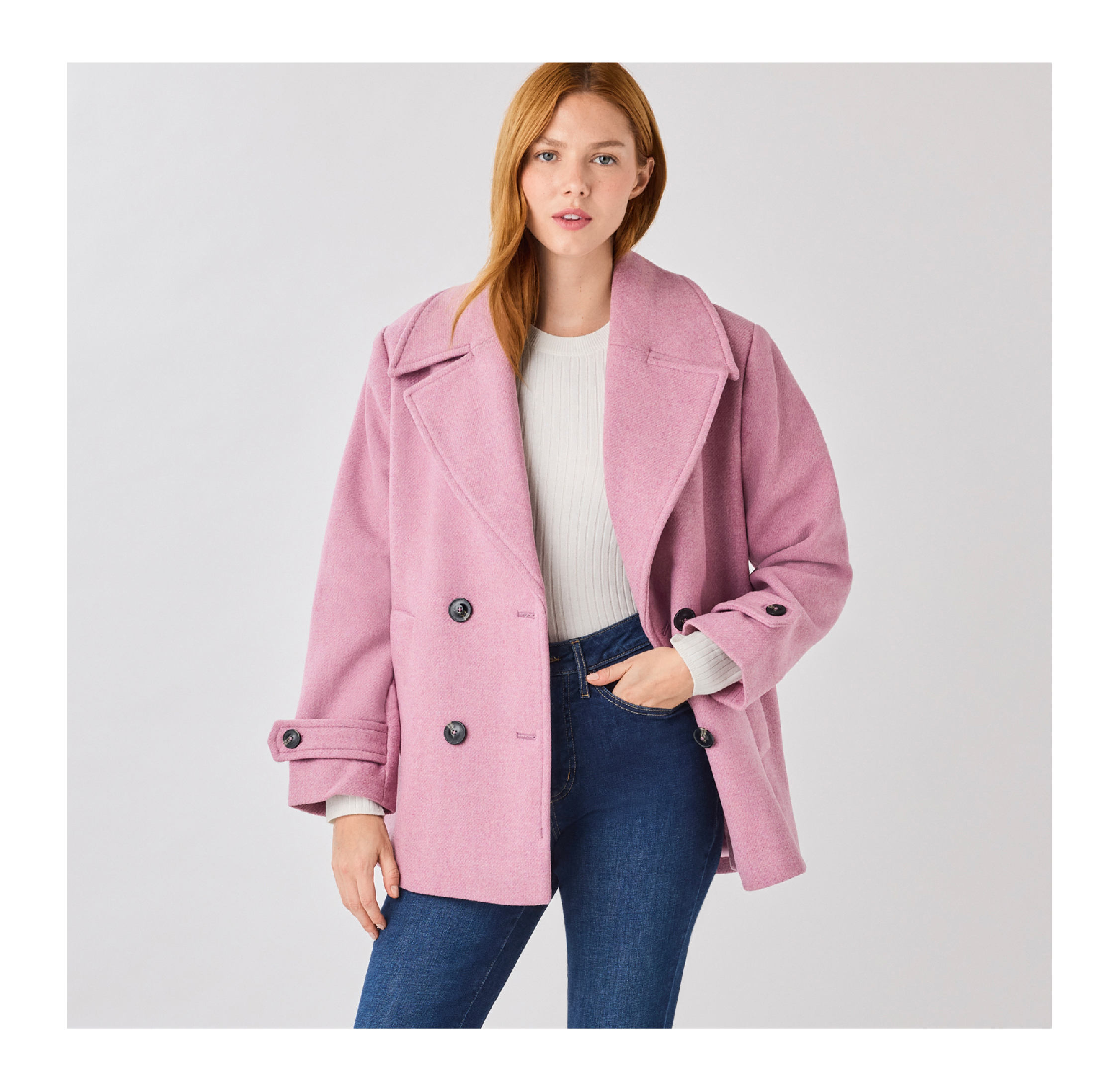 Woman wearing a pink coat and jeans, standing against a light background.