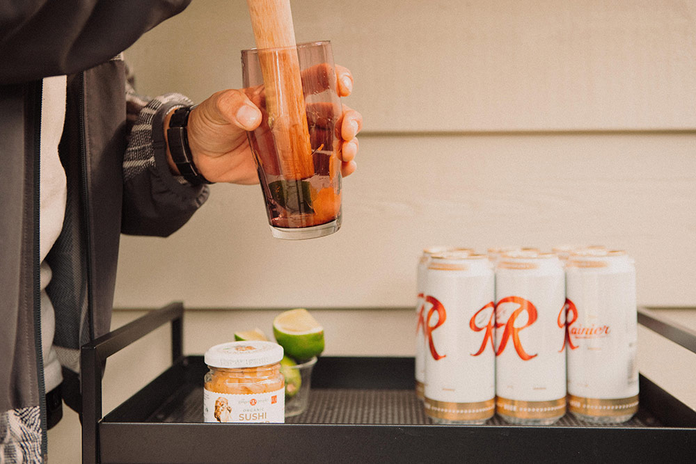 Making a shandy cocktail using a Mazama pint glass and muddling limes and ginger with a 6-pack of Rainer waiting to be used on the bar cart.