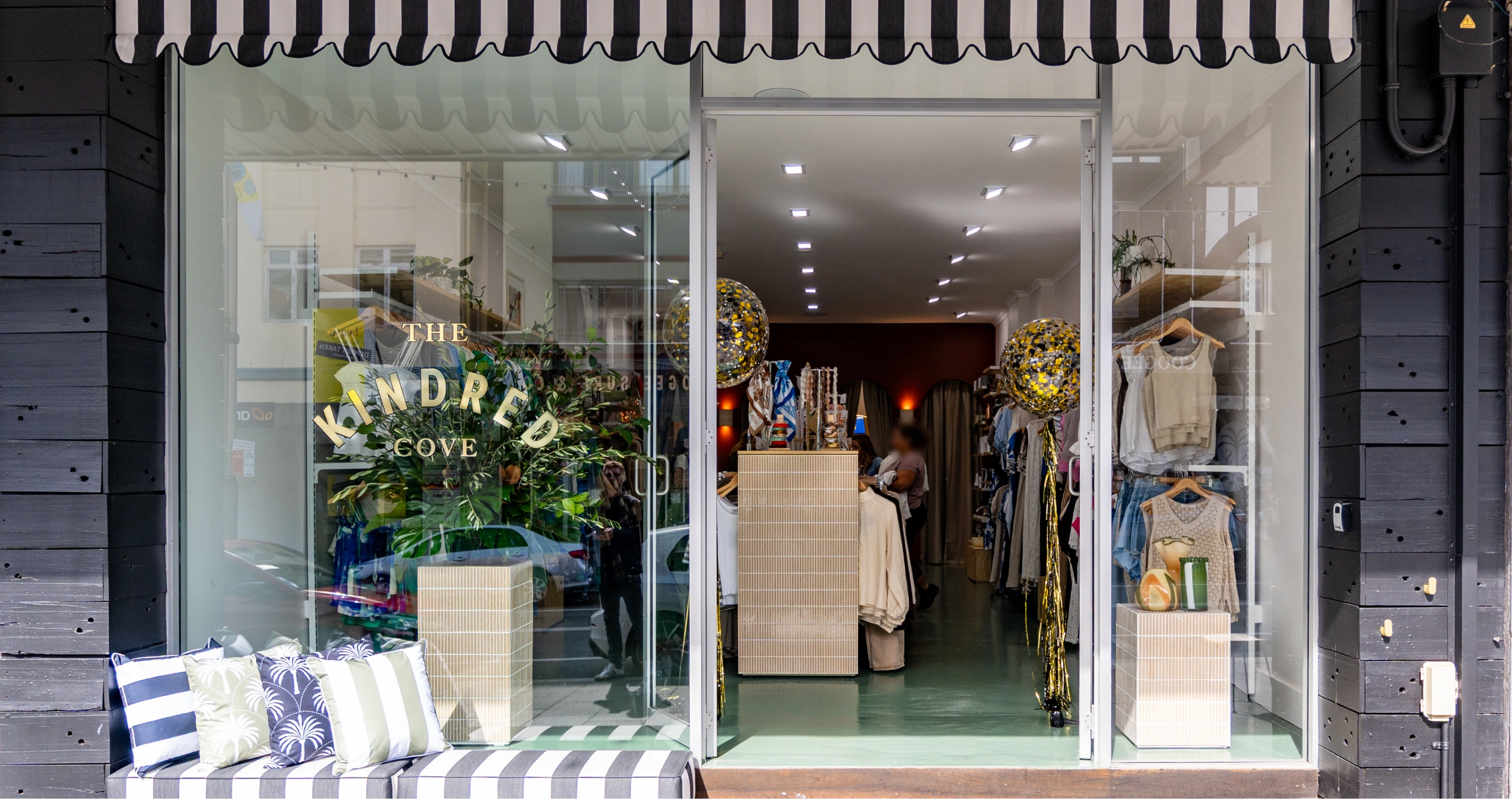 Storefront with glass doors, displaying clothing and decorative items inside.