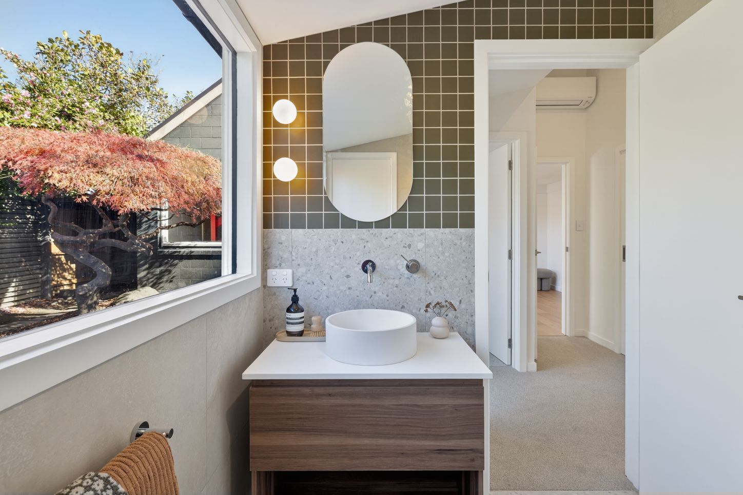Modern bathroom with a sink, mirror, and view of greenery outside.