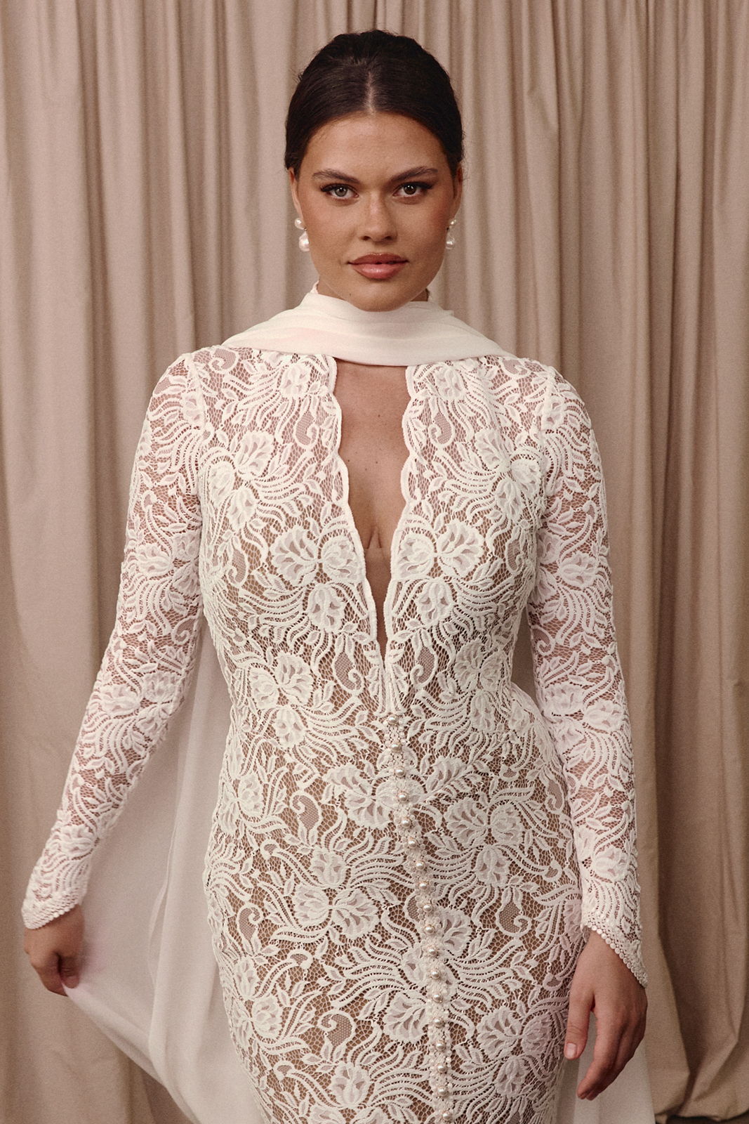 Model wearing a white lace dress with a high neckline and long sleeves.