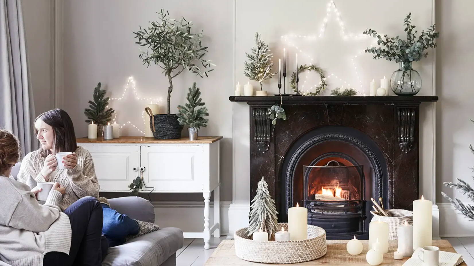 Christmas living room with fireplace and TruGlow candles arranged on coffee table with wreaths,  garlands, mini trees and large Osby star styled in the room