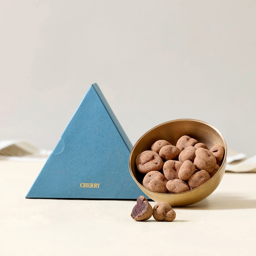 A blue pyramid box next to a bowl of chocolate-covered snacks.