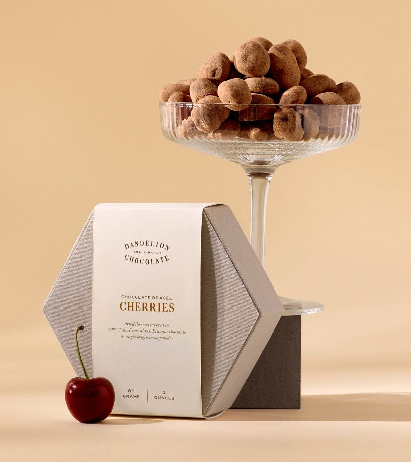 A dessert presentation with chocolate-covered cherries in a glass and a package.
