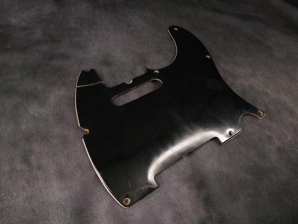 Black guitar pickguard on a dark background.