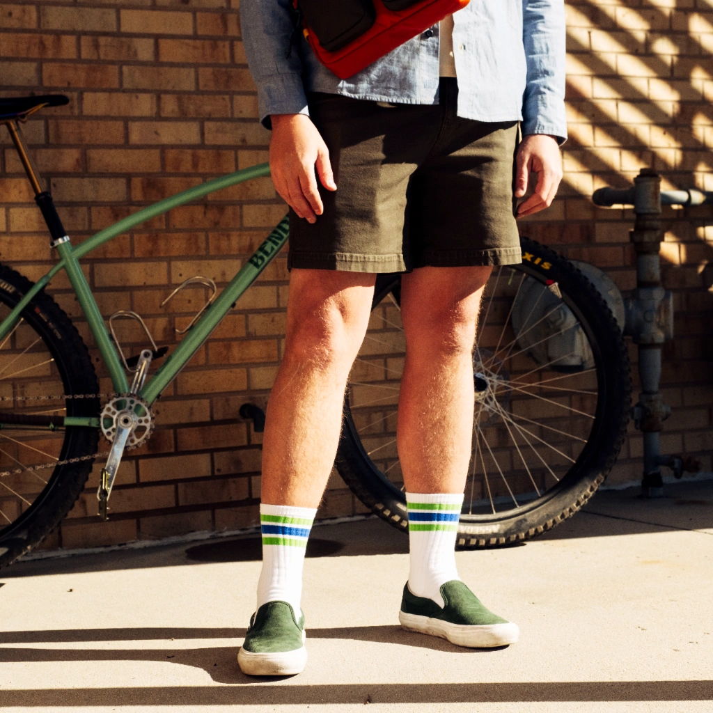 Person wearing shorts, colorful socks, and shoes next to a bicycle.