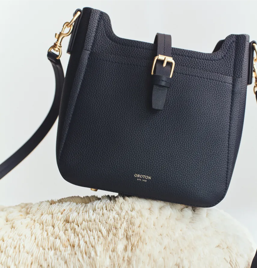 Black handbag with a gold buckle, resting on a soft surface.