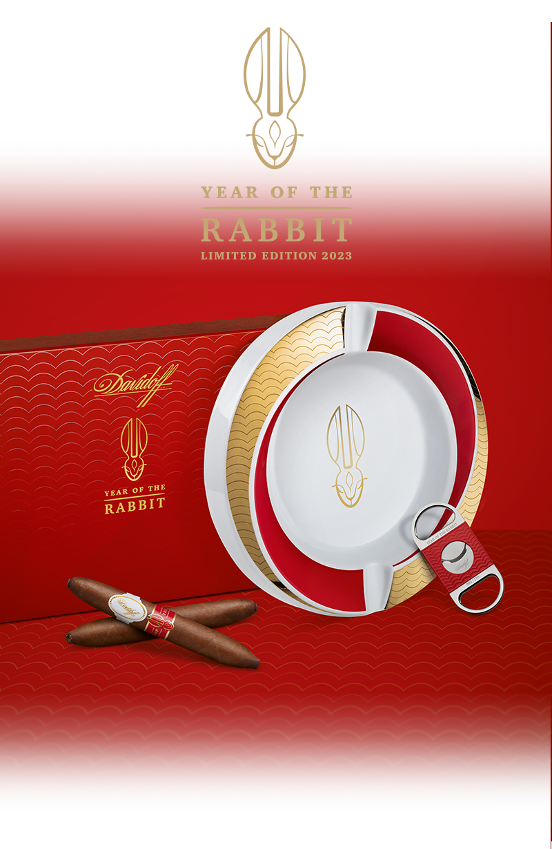 Two Davidoff Year of the Rabbit Limited Edition cigars crossed lying in front of their red box, next to them are the Year of the Rabbit ashtray and the Year of the Rabbit cutter.