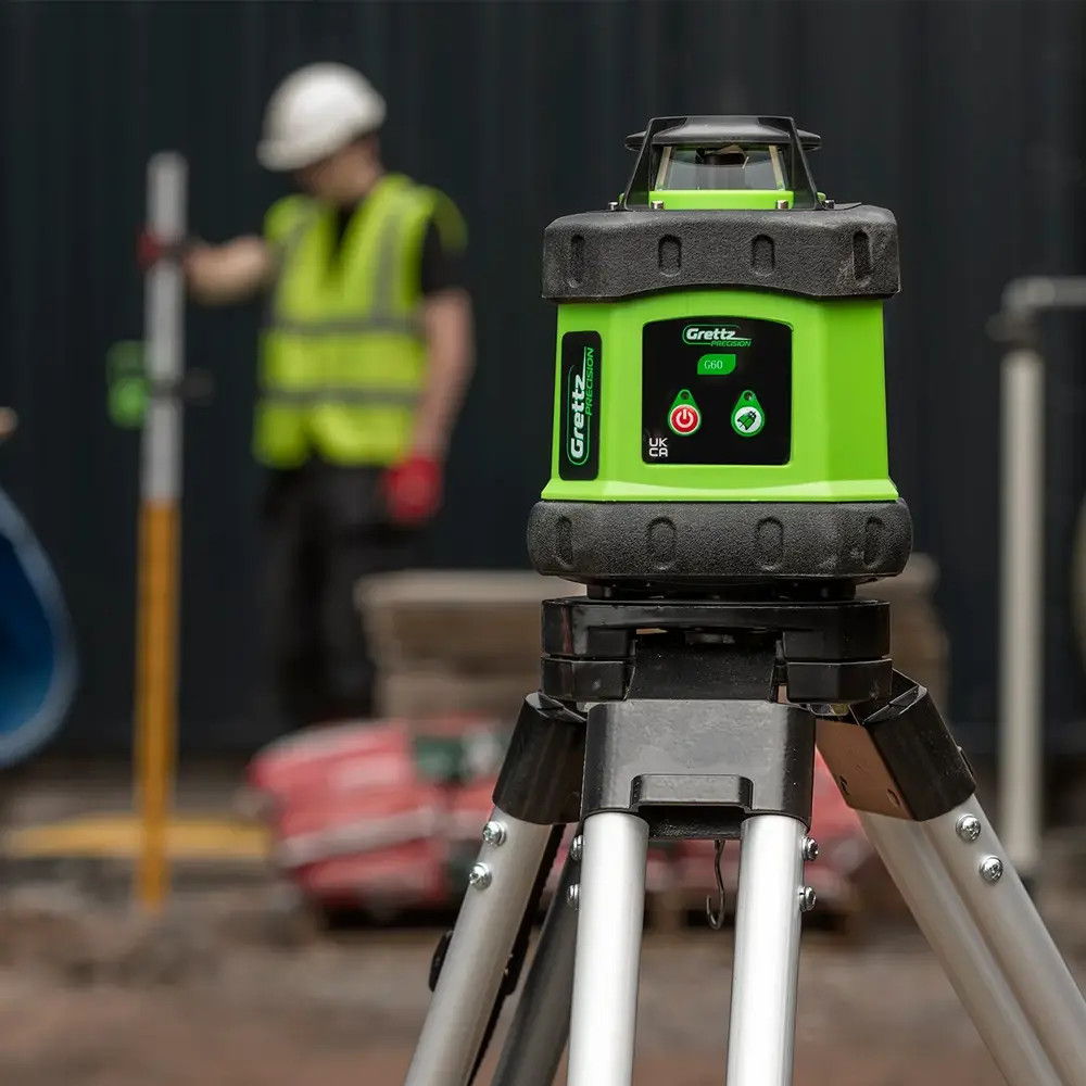 A green laser level on a tripod with a construction worker in the background.