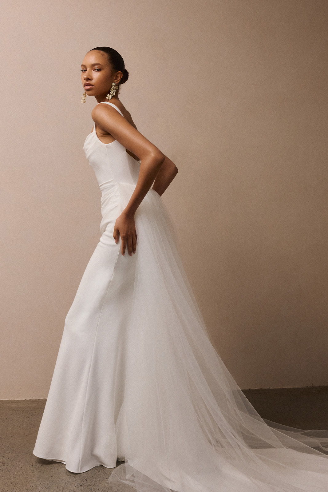 Model wearing a flowing white wedding dress against a neutral background.