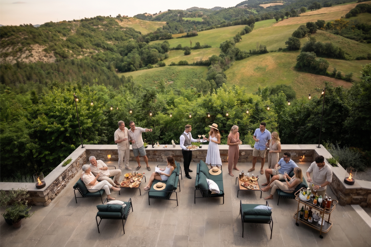 Large patio entertaining zone with lounge seating, small tables, and guests gathering across the space for an outdoor party.