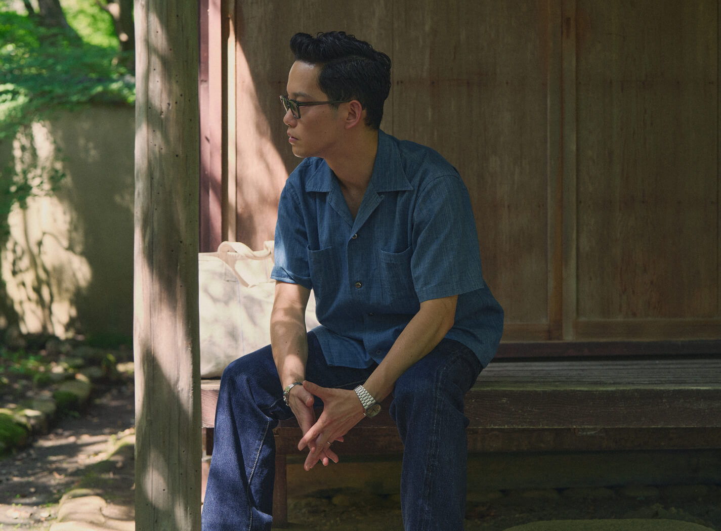 Person sitting on a bench, wearing a blue shirt, in a serene outdoor setting.