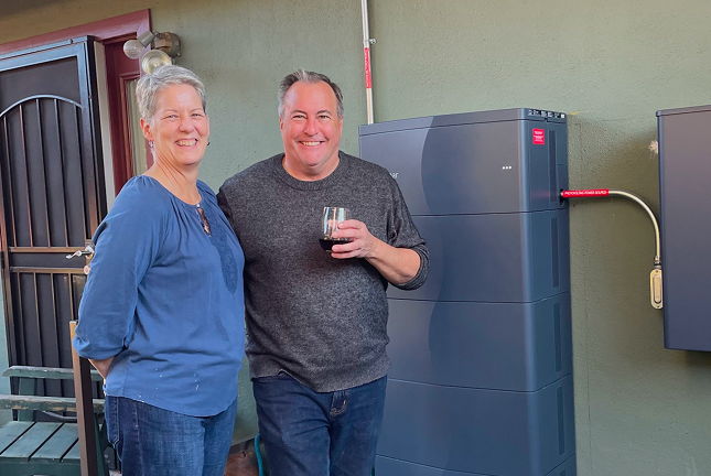 Two smiling people standing next to Lunar Energy ESS home storage system outside their home.