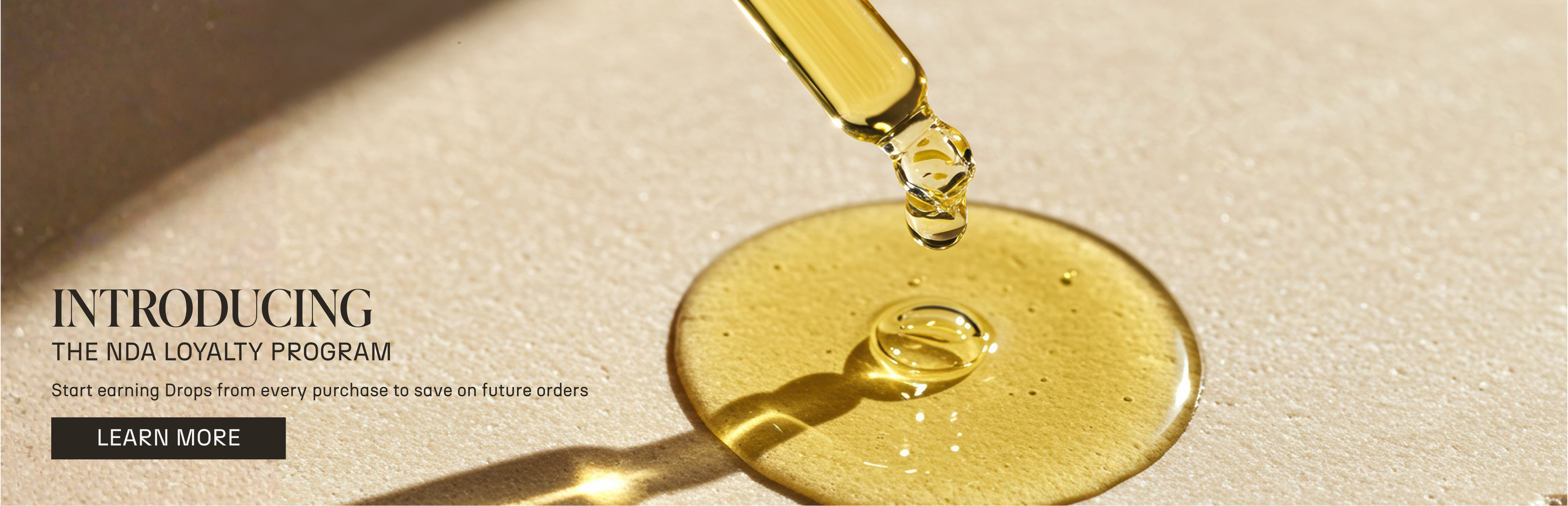Dropper releasing golden oil onto a smooth surface.