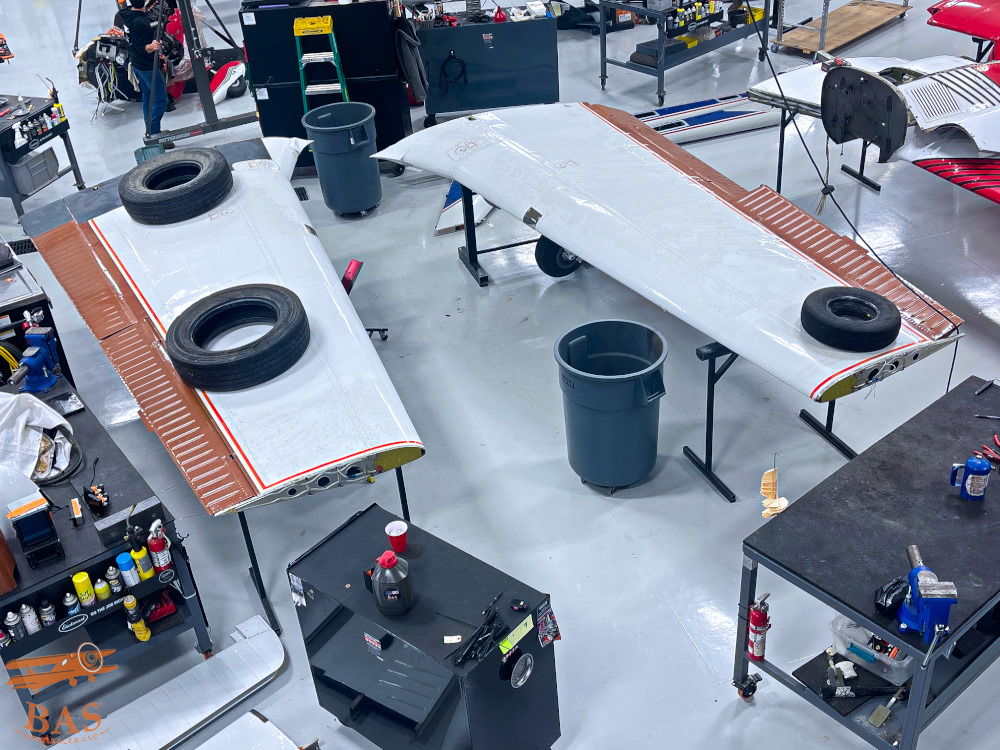 Two airplane wings on work tables in a manufacturing facility.