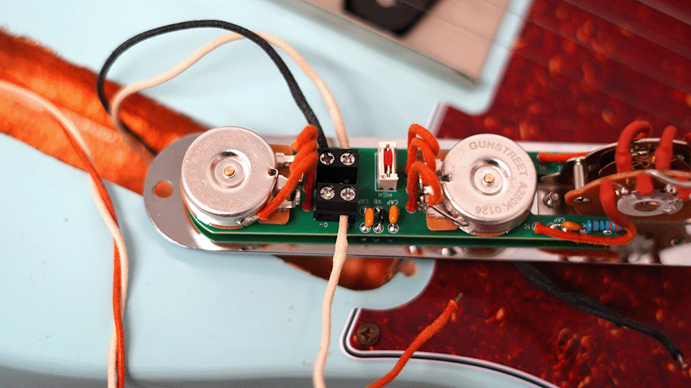 Close-up of guitar wiring and electronic components on a guitar body.