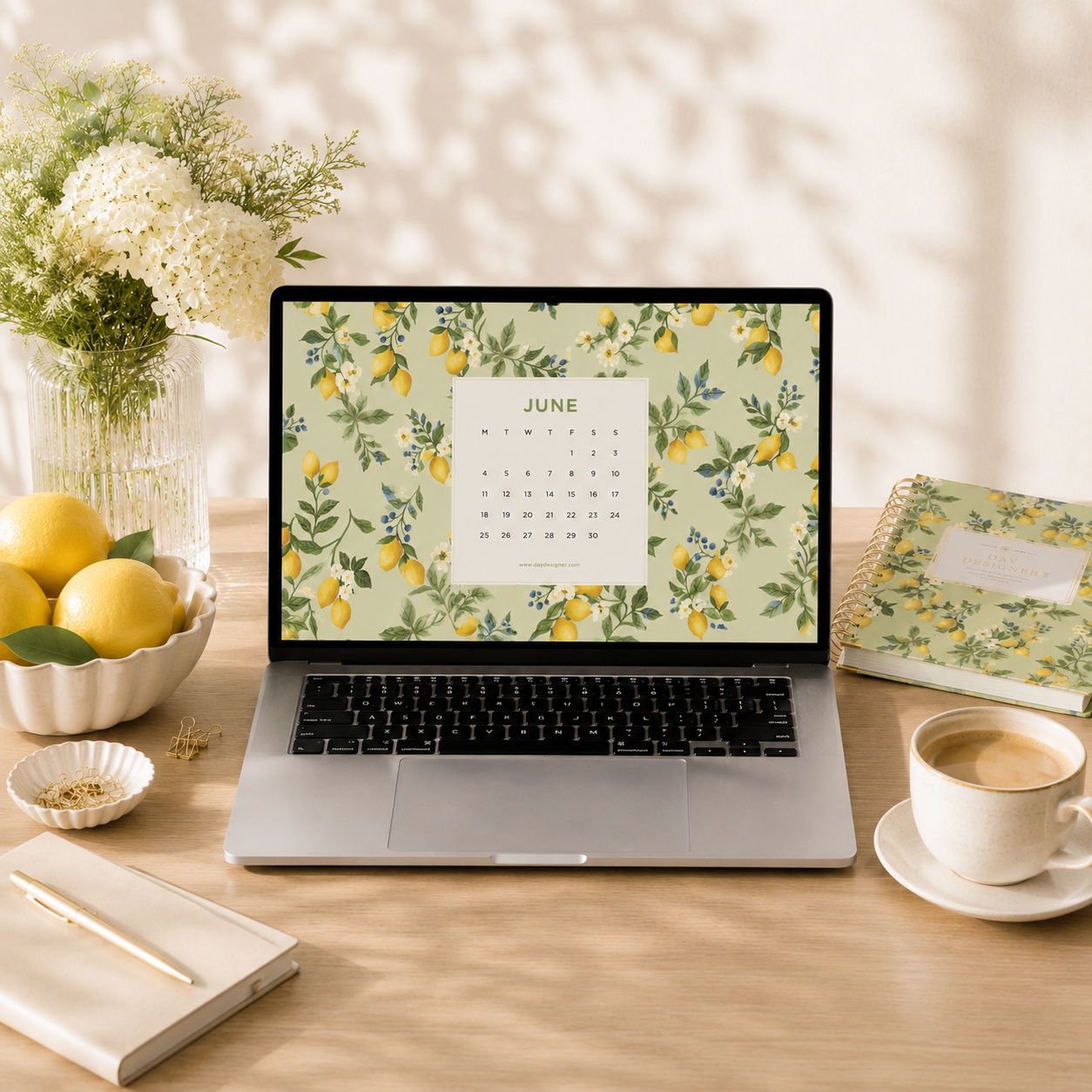 laptop showing june digital wallpaper on a lemon floral background, desk, coffee, planner, book with pen, bowl of lemons, dish with paperclips, vase with white flowers