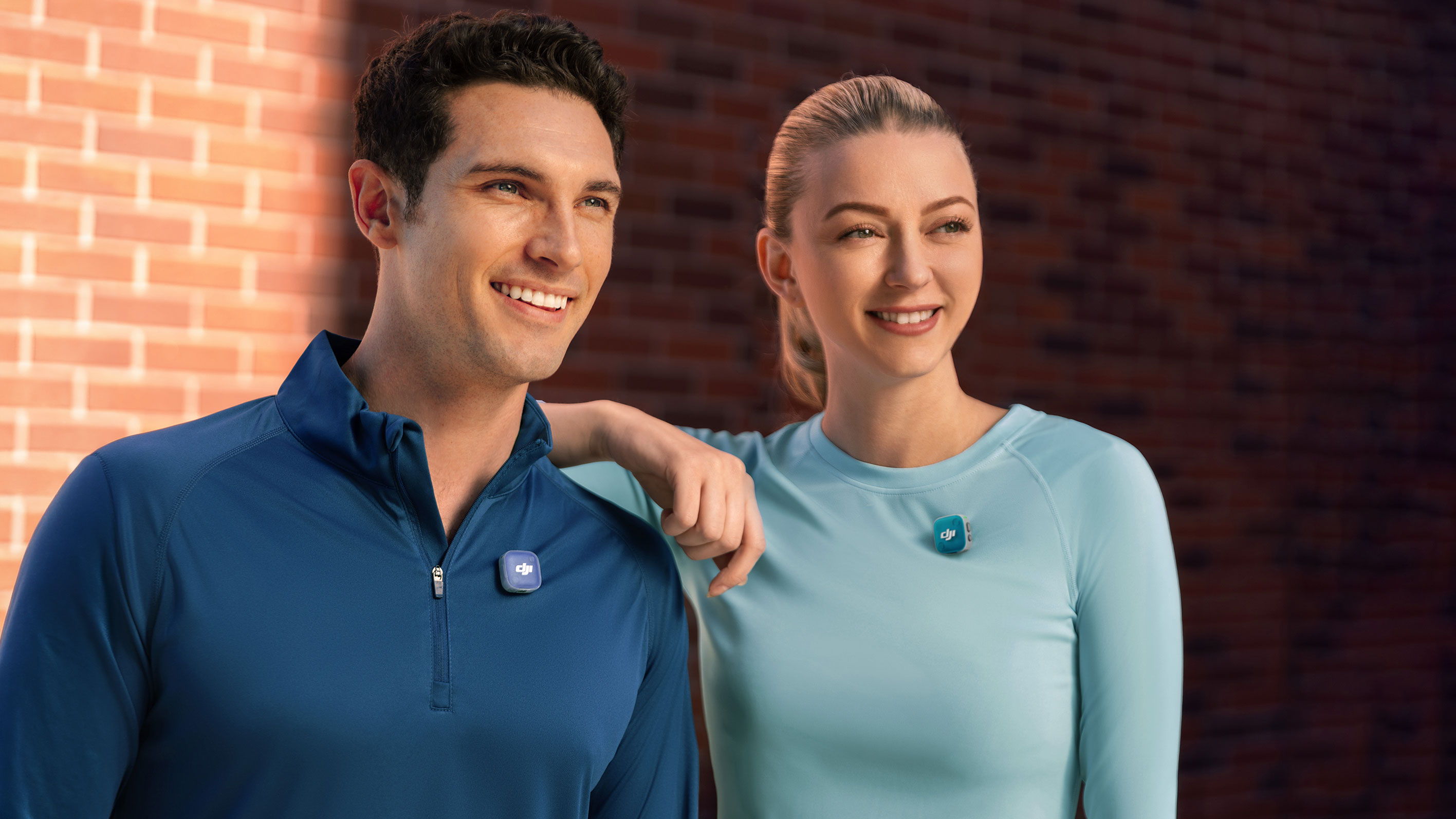 Two smiling people standing together against a brick wall while recording audio with colourful faceplates on DJI Mic Mini 2
