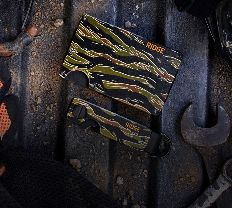 Camouflage wallet on a textured surface with tools.
