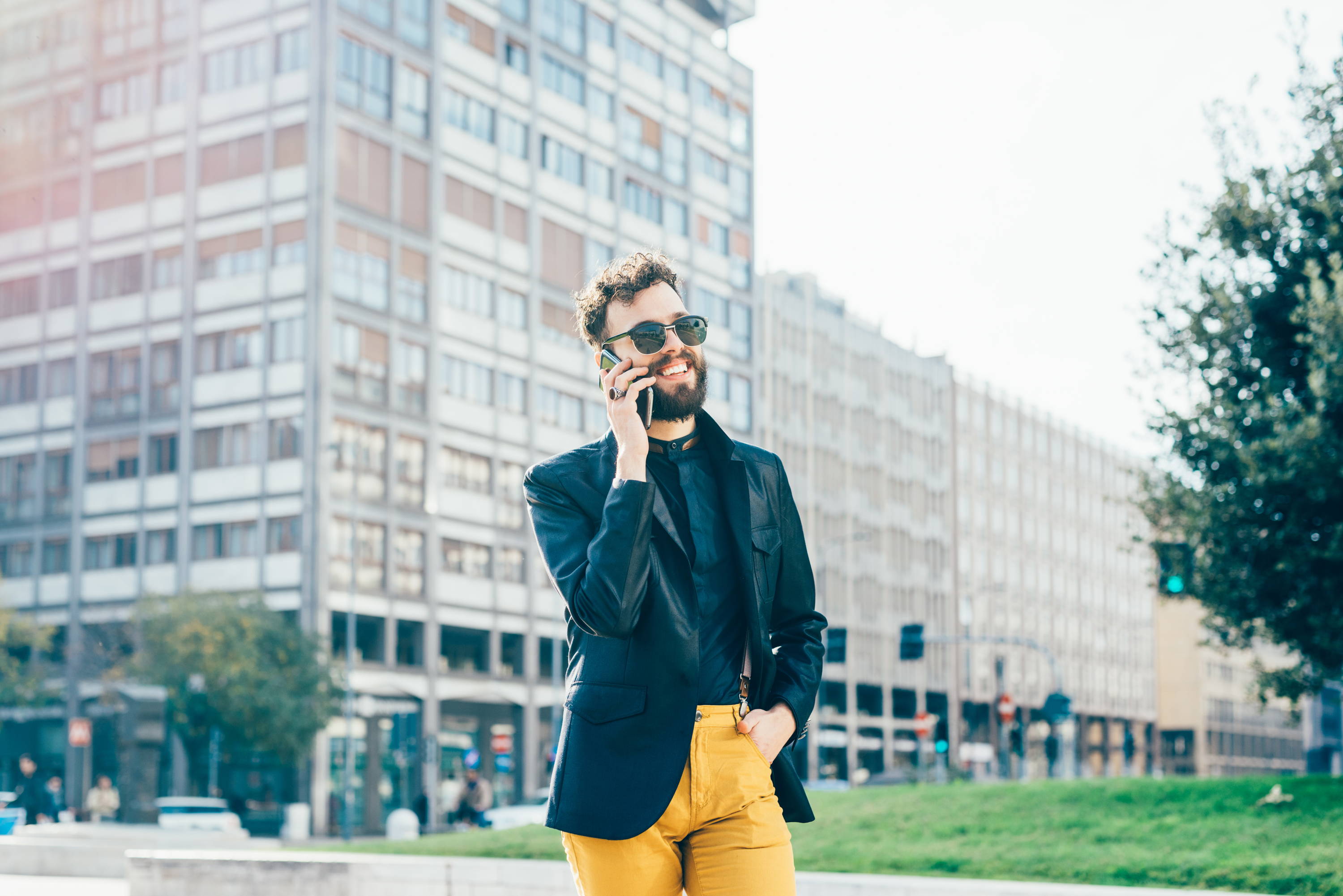 Knee figure of young handsome caucasian bearded man walking outdoor in the city, talking smart phone - communication, business, happiness concept