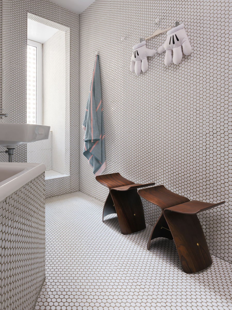 Modern bathroom with patterned tiles, wooden Butterfly stools, and hanging towels.