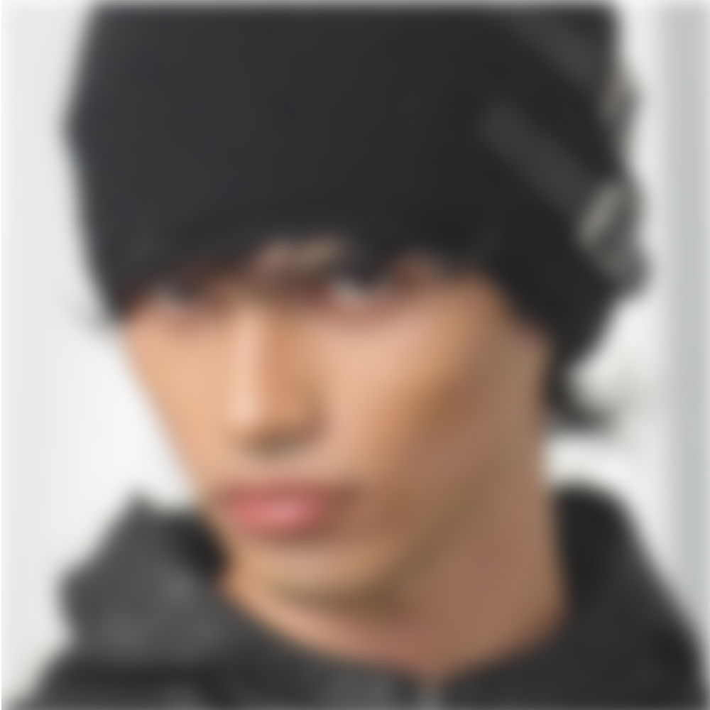 A blurred portrait of a young man wearing a black beanie.