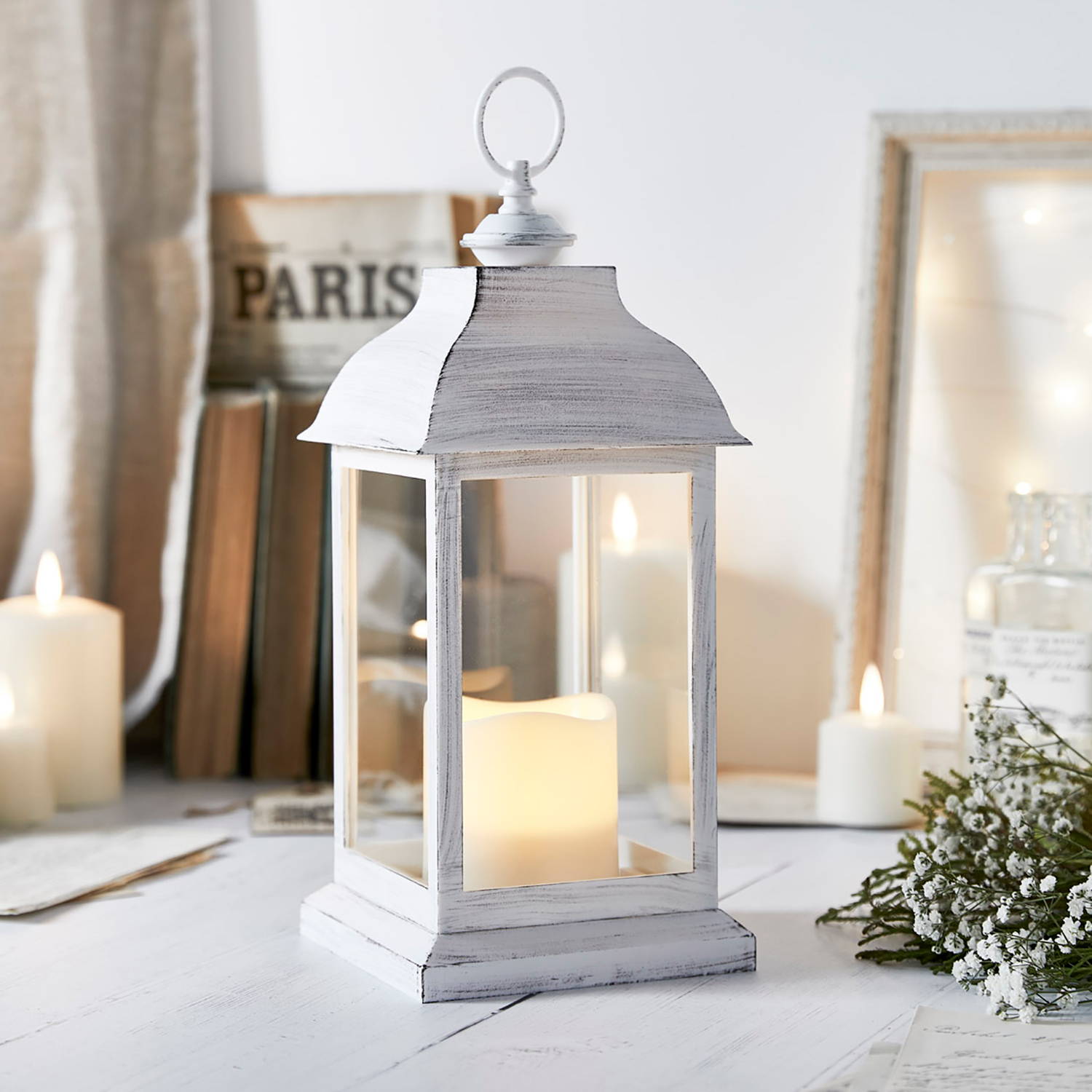 A white wooden lantern with an LED candle on a bedroom side table.